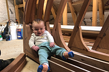 A baby boy lying smiling among stacked frames of a boat hull