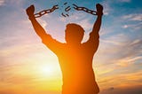 A shadowy photo of a man breaking his shackles with the sun and the sky in the background.