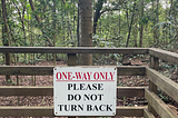 A sign nearing the end of the hiking trail reads in red and black bold, uppercase letters, “ One-way only” and “Please do not turn back.”