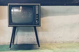 An CRT television on peg legs sits against a white industrial-looking wall.