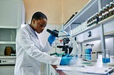 African American biochemist working with microscope during medical research in laboratory.