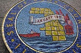 Cook County seal mosaic in Cook County Board Room. image of a boat on water, the outline of cook county government district, municipal buildings, and a banner with January 1831.
