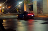 a midnight blue sports car (Porsche maybe) speeding down the empty city streets, after midnight.