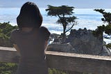 Me, standing by the ocean, looking out at the water and the Lone Cypress in Pebble Beach, California on a quiet, sunny day.