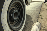 An old Chevy with flat tire and an ominous man’s shoe next to it