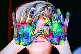 Child with multicolored paint on hands.