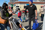 NYC DCWP street team member distributes an NYC Free Tax Prep flyer about claiming tax credits to a parent pushing a stroller in Brooklyn during the 2022 tax filing season.
