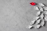 A paper boat in red is in front of three lines of white paper boats, indicating that they’re following it.