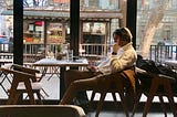 A person in a chair in front a window on a phone, looking at another phone. What are you doing and why are you doing it?