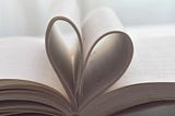 a book sits open and in profile; the middle pages are folded inwards to create a heart-shape