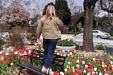 A woman standing on a bench in a park, surrounded by tulips