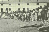 Photo of formerly enslaved people standing in front of barracks at Camp Barker in Washington DC, 1862
