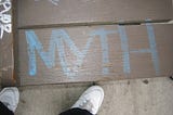 “Myth” written on the ground in blue color with white colored shoes besides it.