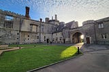 The exterior of Thornbury Castle near Bristol, England, featuring the fountain courtyard, late afternoon sun and a blue sky. Photo by Laura Metze.