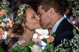 A bride and groom kiss with their eyes closed and framed by small white and peach colored flowers.