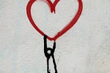 Ink-drawn stick person hanging from the bottom of a red heart.