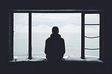 A gentleman sat looking out over window peacefully as a silhouette.