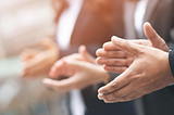 Two professional-looking men and a woman in a suit are clapping hands