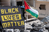 Black Lives Matter flag alongside a Palestinian flag in the rubble of a destroyed building