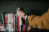 person picking white and red book on bookshelf