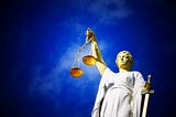 Lady justice holding the scales of justice in her right hand and a sword in her left, set against a blue sky background.