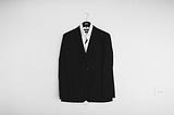 A suit, hung up against an unadorned white wall.