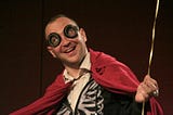 Cory Doctorow, a white male, in goggles and a red cape with a very large, slightly creepy smile.