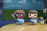Funko Pop Bob Ross and Deadpool Bob Ross figurines placed in an art studio in front of a large 4 panel painting as inspiration for the artist herself. Which is me. Kathy LaFollett. Kathy LaFollett Murals and Canvas