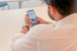 Photo of a man from the back while he is sitting in a desk looking through and article on his phone