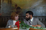 A man and a woman sit at a table with a bouquet of flowers before them.