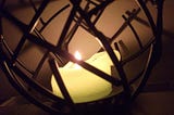 white candle burned down sitting in a dark wooden, circular cage.