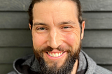 A photograph of Patrick Beukema, a man with brown hair and a brown beard wearing a grey hoodie.