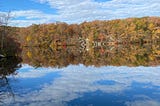 The changing colors of leaves are reflected in a lake. Photo by author.