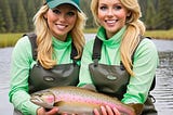 Two blonde women in waders holding a rainbow trout