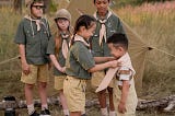 Children dressed in scout uniforms. A girl is helping a little boy tie his neckerchief.