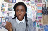A black girl sitting in front of a wall plastered with anime illustrations and memorabilia.