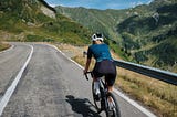 A woman riding a road bike along a long mountain road.