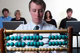 Image of man using abacus while everyone else is using a computer