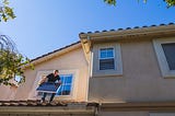 A man holding a solar panel on the roof of a house.