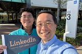 Two men in front of LinkedIn office building holding a sign that says “LinkedIn est. 2023"