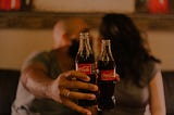 Two people hold up Coca-Cola bottles.