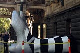 Giant feet, wearing silver shoes and striped socks, emerging from a building.