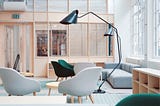 An office lounge area with blue rugs, grey and green chairs and a modern grey couch