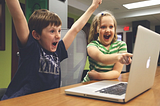 A photo of two happy, excited children pointing to a computer display.