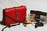 A selection of luxury branded consumer products: handbags by Prada and Yves Saint Laurent, perfume by Chanel, and expensive jewelled earrings.