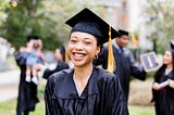 A smiling young woman graduating college in her black cap and gown.