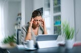 Young woman working from home, holding head in pain with room spinning