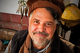 Image of H. Bruce Rinker, Ph.D smiling, in his livingroom behind him a globe and a native american dream catcher.