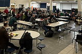 Nearly 100 people sit in a middle school cafeteria for a community meeting.