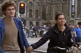 Two bike riders with out helmets holding hands, with bikes in the background.